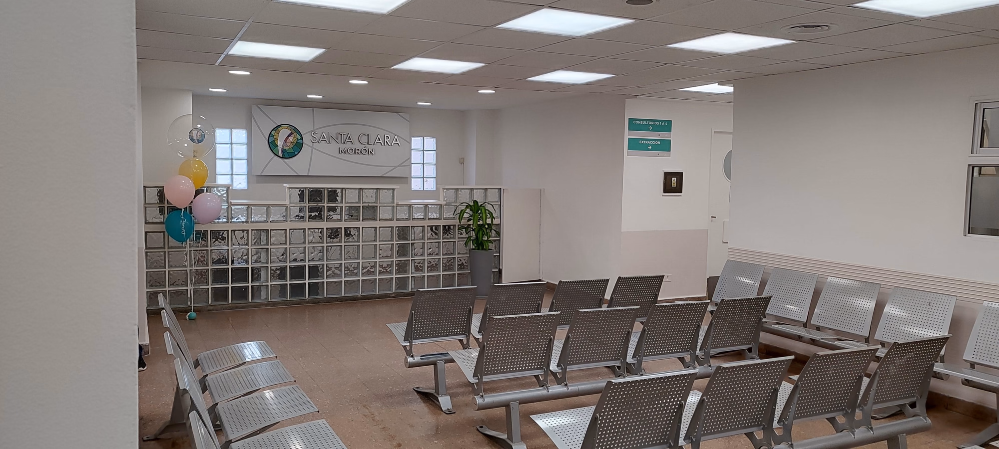 Sala de espera de la Clínica Santa Clara en Morón, con asientos enfrentados y logo institucional