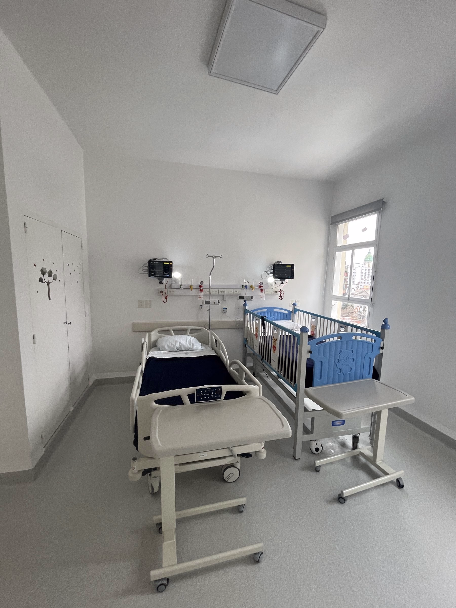 Habitación de pediatría del Centro Gallego con cama junto a la ventana y equipamiento clínico