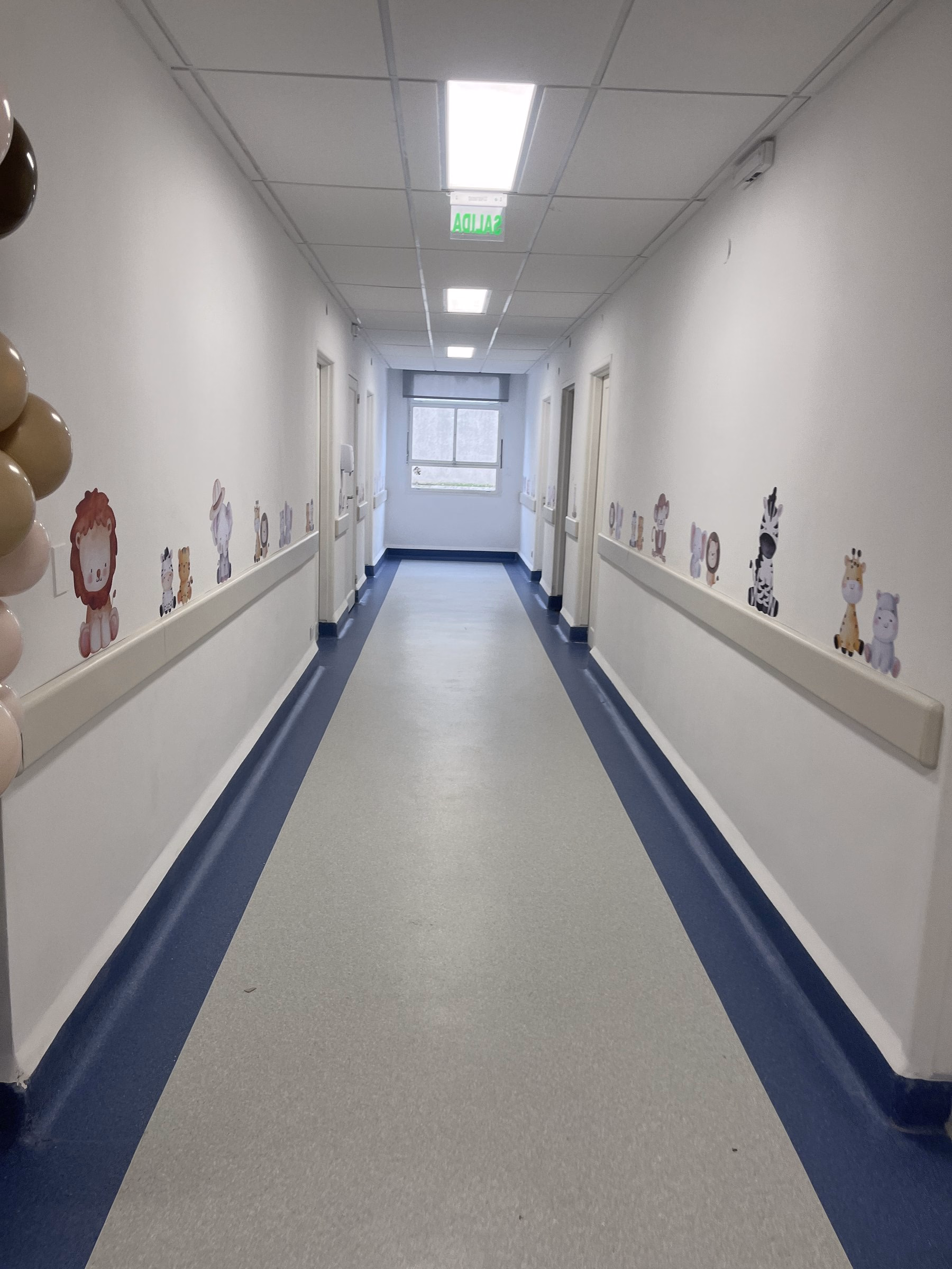 Pasillo de pediatría del Centro Gallego, con zócalo azul y gráficos en la pared